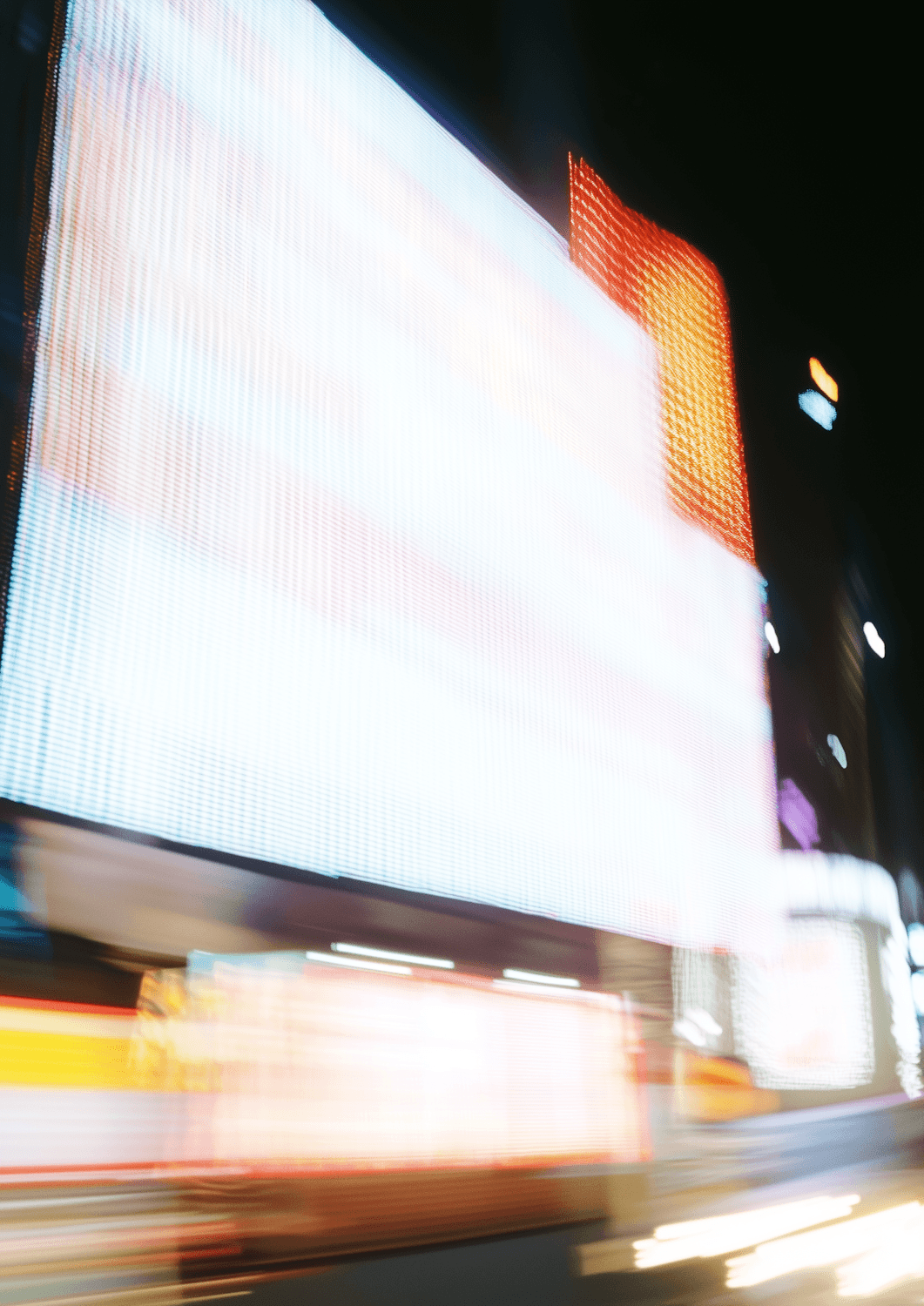 Streaks of light and glowing screens on a busy evening street